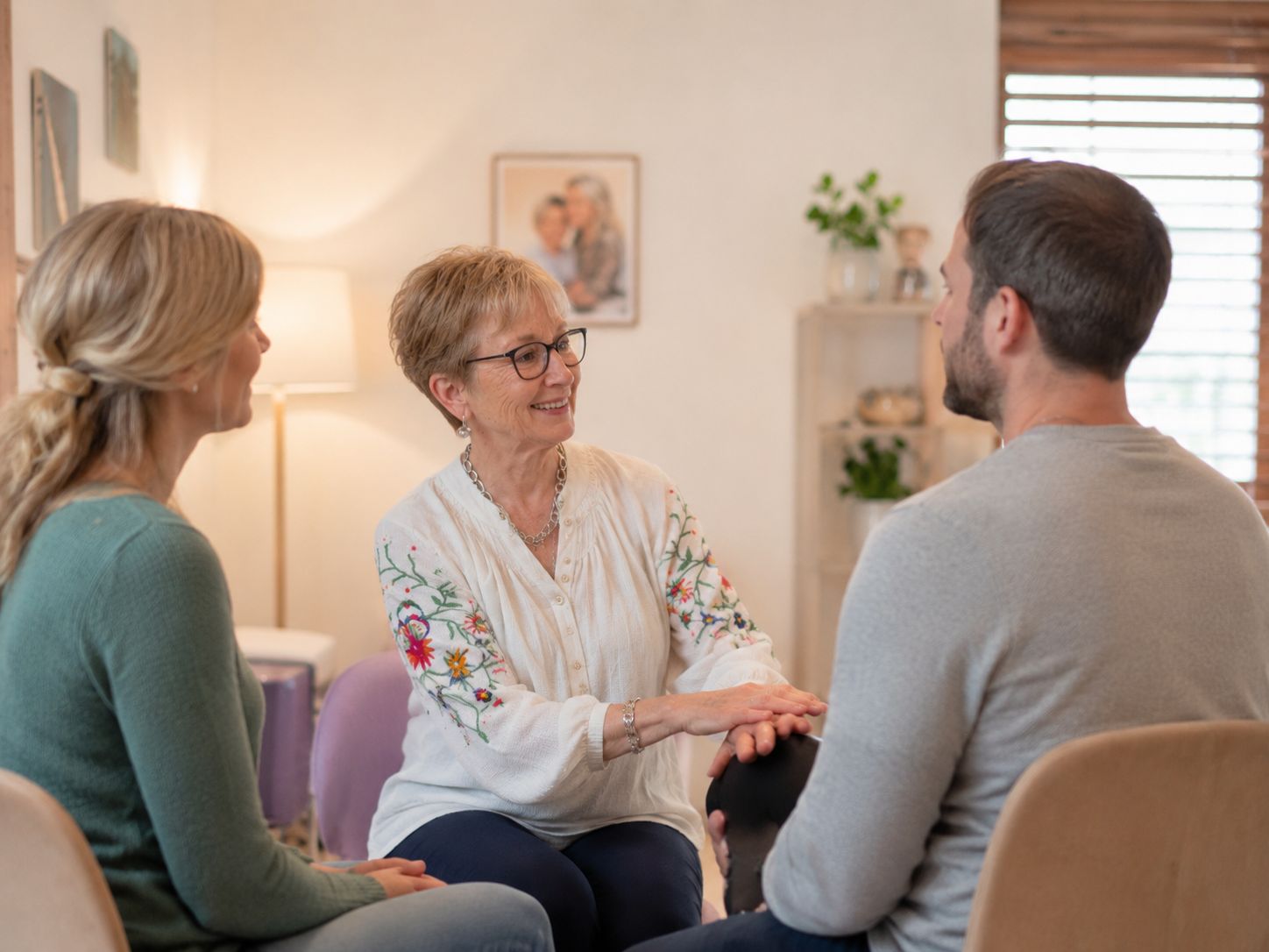 A physical therapist speaks warmly with a couple during a consultation in a calm, home-like room.